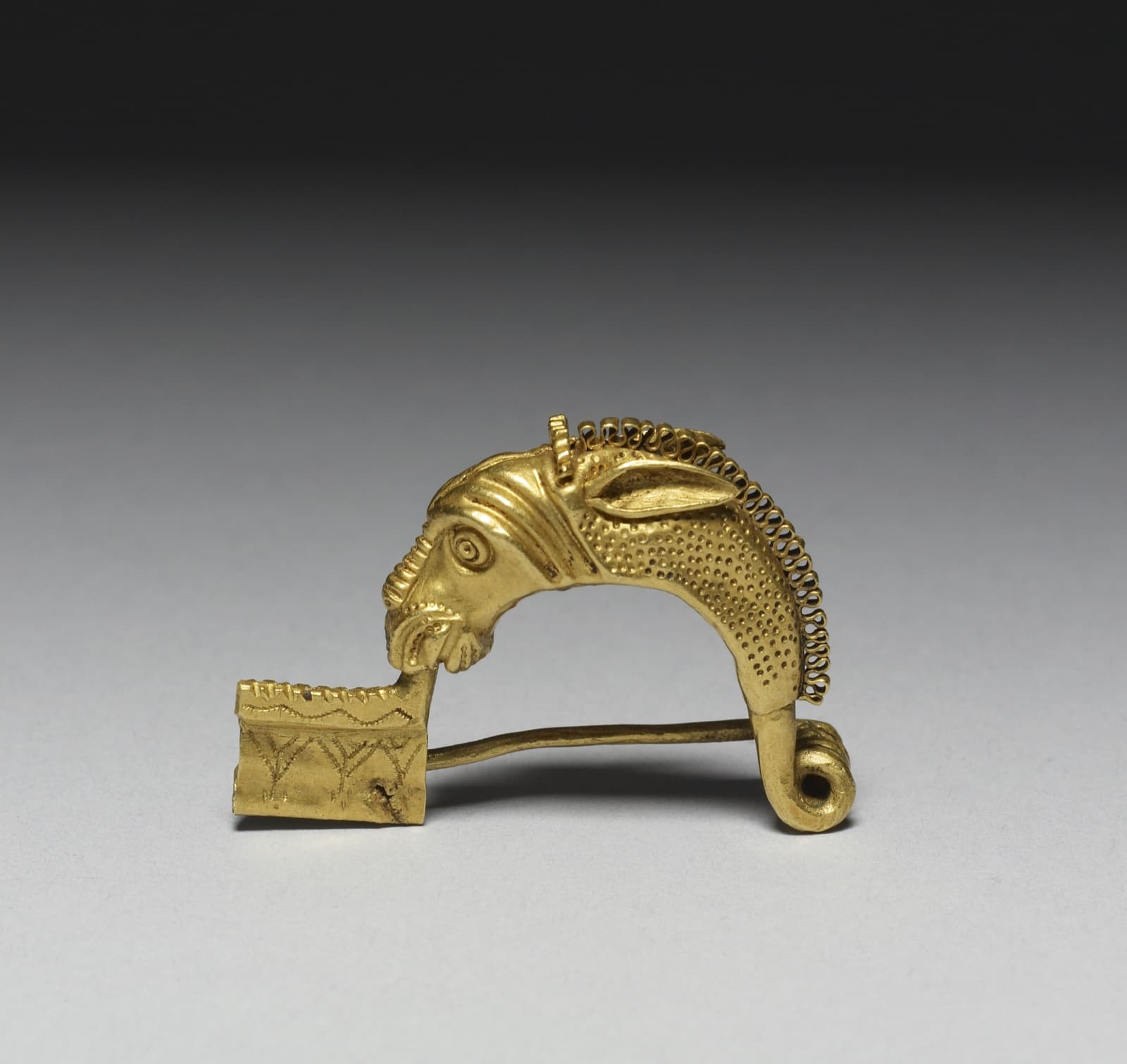 Small gold brooch shaped as a horse's head, with a filigree mane and a coat of punched dots