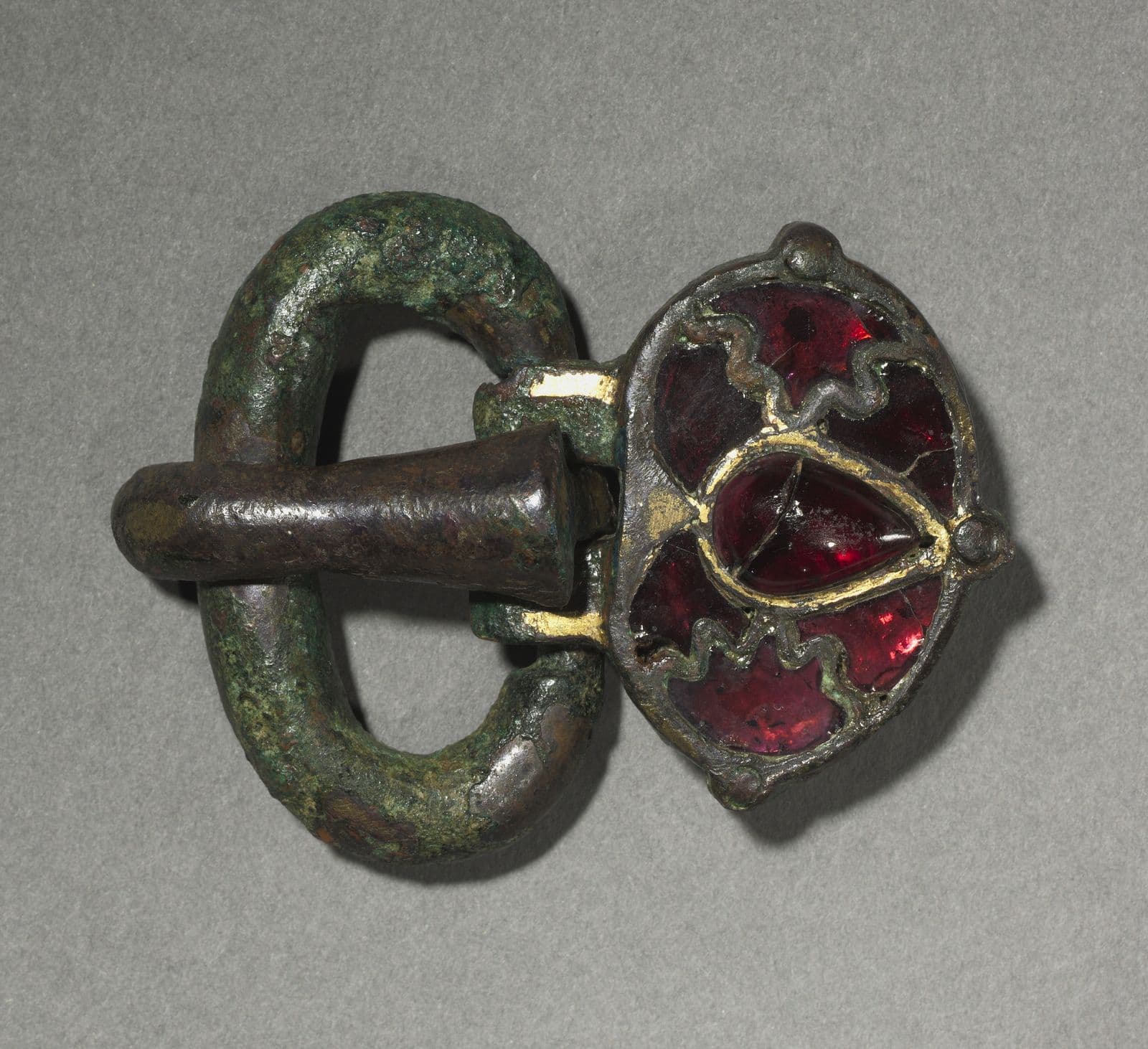 Bronze belt buckle with traces of gilding, set with red garnet stones, corroded green with age