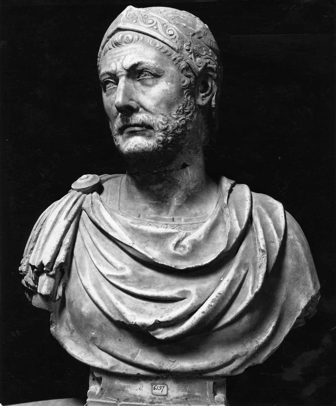 Black-and-white photograph of a marble bust of a helmeted man with a beard, photographed against a dark background